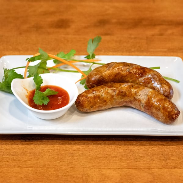 Two grilled Sticky Rice Bites sausages with a side of red dipping sauce and cilantro garnish.