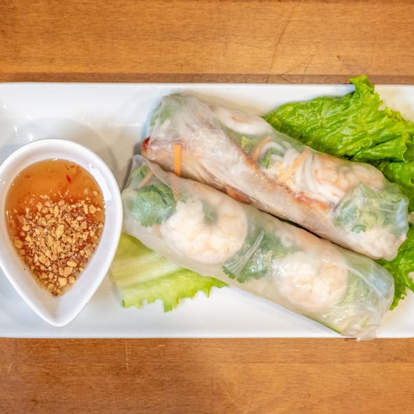 Two fresh spring rolls with shrimp and vegetables, served with peanut sauce and lettuce.