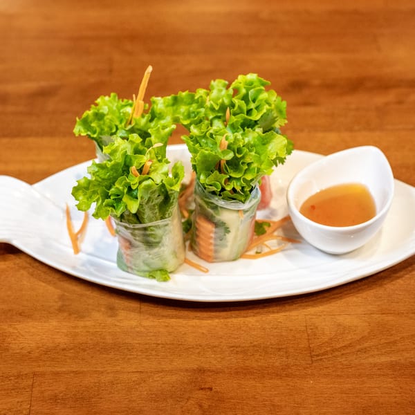 Fresh spring rolls with lettuce, carrots, and a side of dipping sauce on a fish-shaped plate.