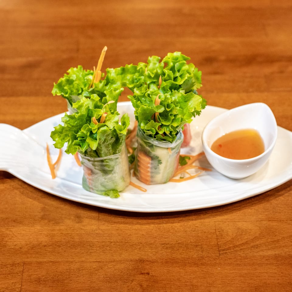 Fresh spring rolls with lettuce, carrots, and a side of dipping sauce on a fish-shaped plate.
