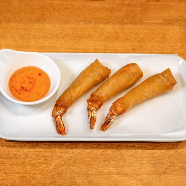 Three golden-fried shrimp spring rolls with visible tails, served with a sweet chili dipping sauce.