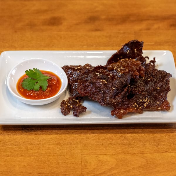 Sticky Rice Bites' crispy beef jerky with sesame seeds and a side of chili sauce with cilantro.