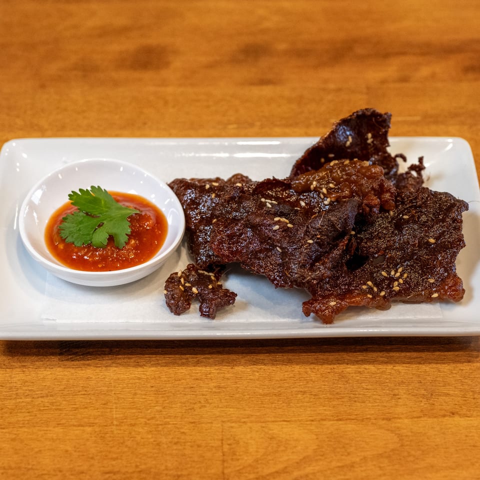 Sticky Rice Bites' crispy beef jerky with sesame seeds and a side of chili sauce with cilantro.