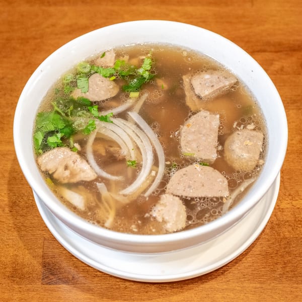 A bowl of Vietnamese pho with meatballs, noodles, and herbs in a rich broth.